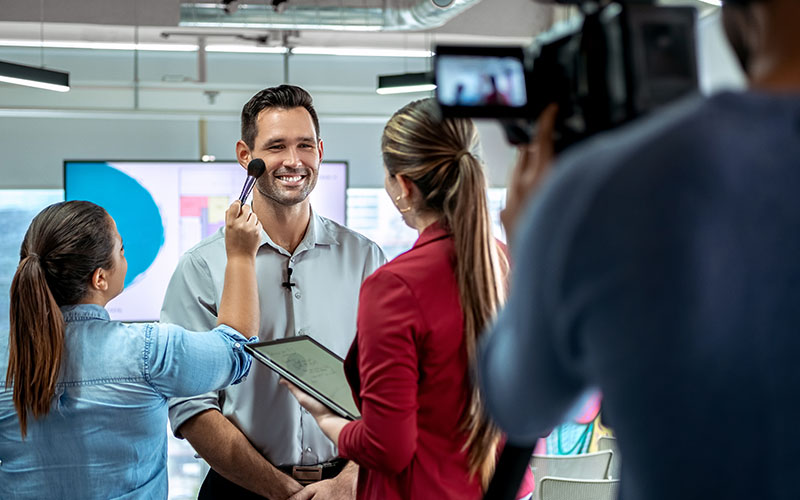 Happy businessman during corporate interview with journalist. Vip or manager talking and smiling in office. Woman at work as makeup artist with business man and cameraman shooting video with camera