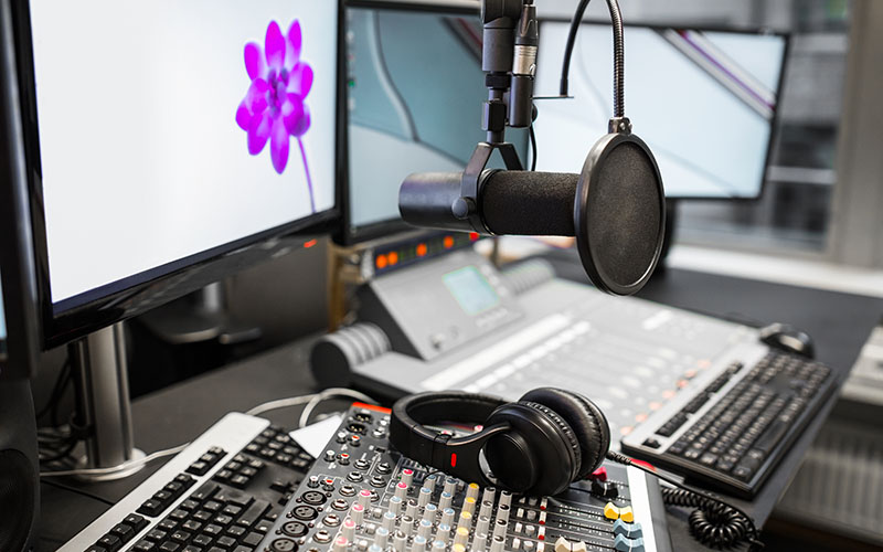 Closeup of microphone with music mixers and headphones by monitors on table in radio studio