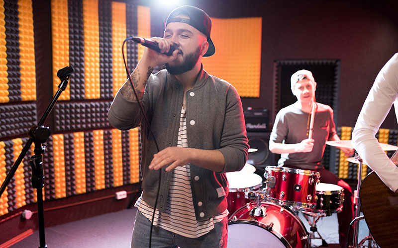 Portrait of modern hip-hop singer performing with his band in recording studio while making new album.