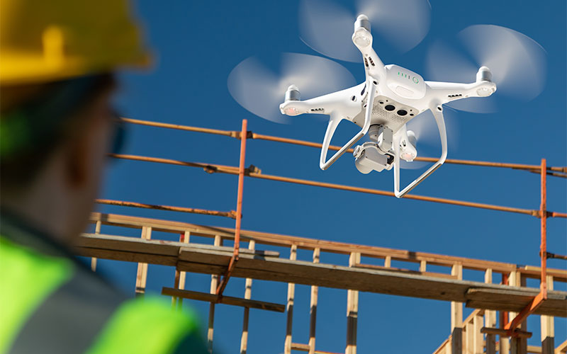 drone; construction site; inspecting; above; inspector; inspecting; photographing; house; quadcopter; construction; uav; home; unmanned aircraft system; real estate; flying; air; aircraft; technology; flight; site; building; industrial; outdoors; outside; framing; girl; pilot; woman; female; worker; safety; vest; hardhat; helmet